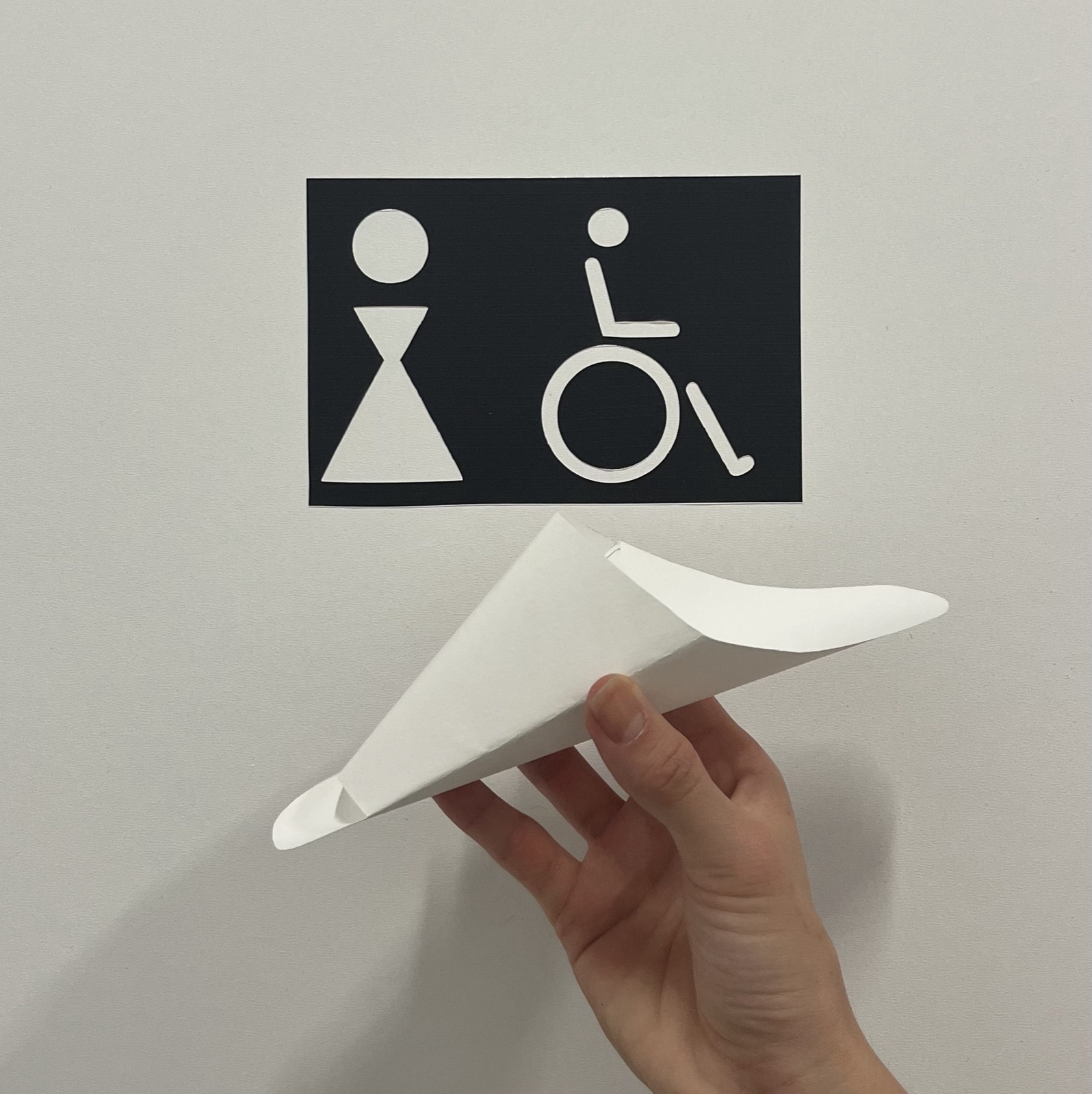 Le dispositif Easy Peezy tenu devant une signalétique toilettes et accessibilité